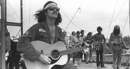 Country Joe McDonald plays for 300,000 people at Woodstock. He said, “They found a guitar, a Yamaha FG 150, and tied a rope on it (see the photo) and pushed me on stage. The rest is history.” Photo credit: Jim Marshall