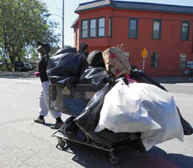A recycler in Oakland hauls a heavily loaded shopping cart. Women recyclers are very vulnerable on the street. Lydia Gans photo