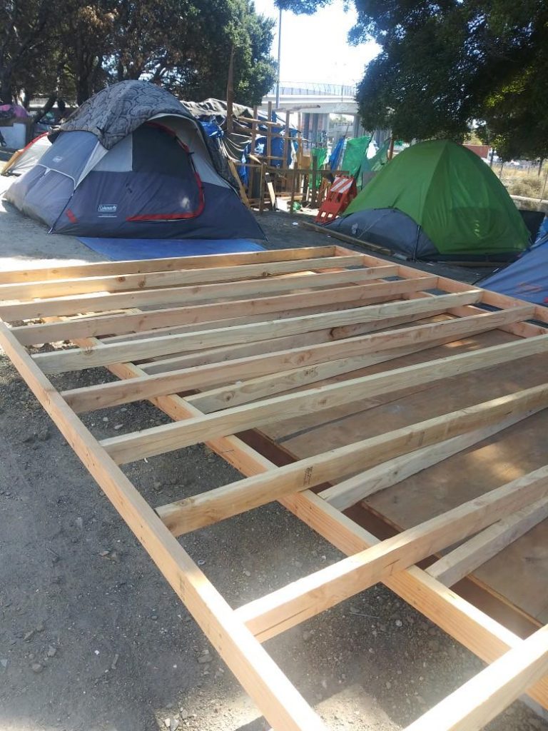 The photo depicts construction of supports in between tents at a homeless encampment in East Oakland