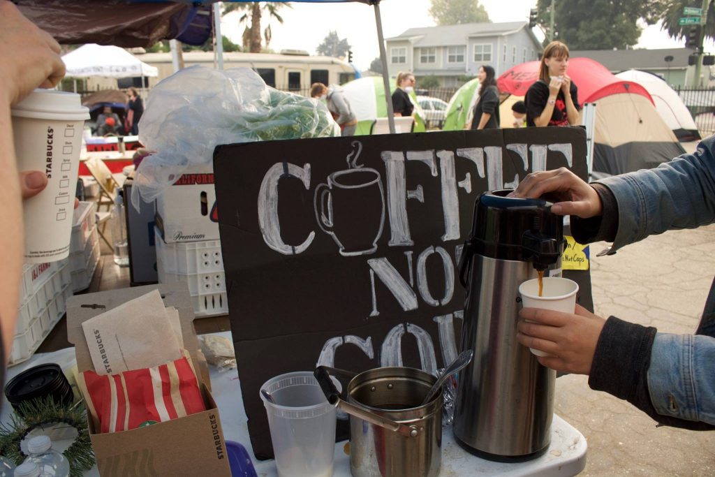A sign reads "coffee not cops" in front of a coffee dispenser. Encampment supporters pour coffee on the day of the eviction.