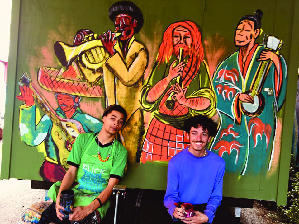 Omari Scott and Jordan Foster sit in front of a mural they painted on the side of one of the tiny houses.