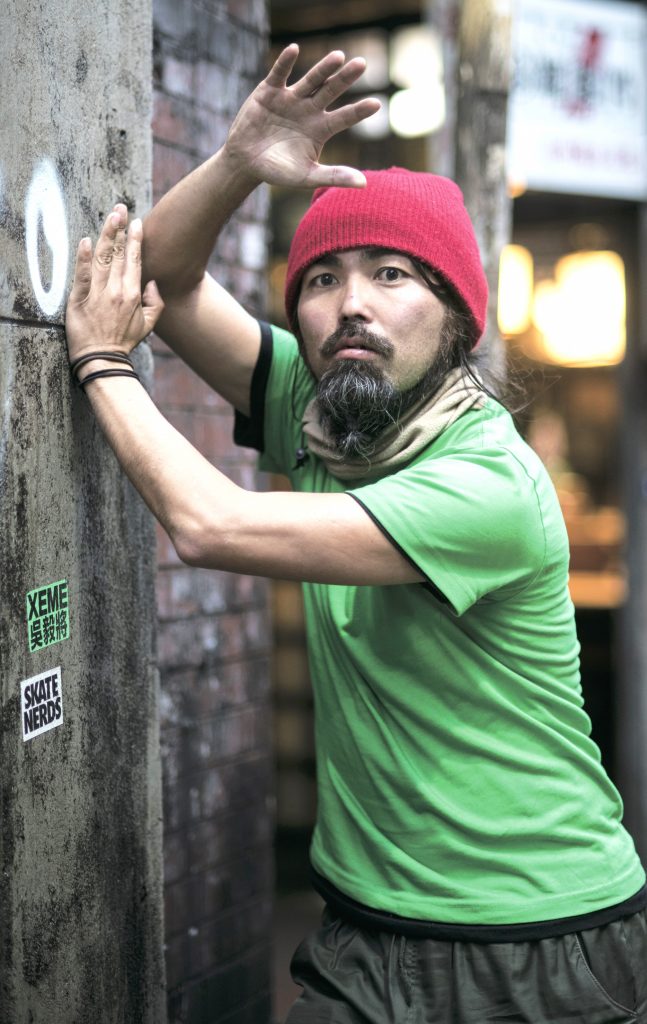 Nishi strikes a pose. He is wearing a green tshirt and a red beanie.