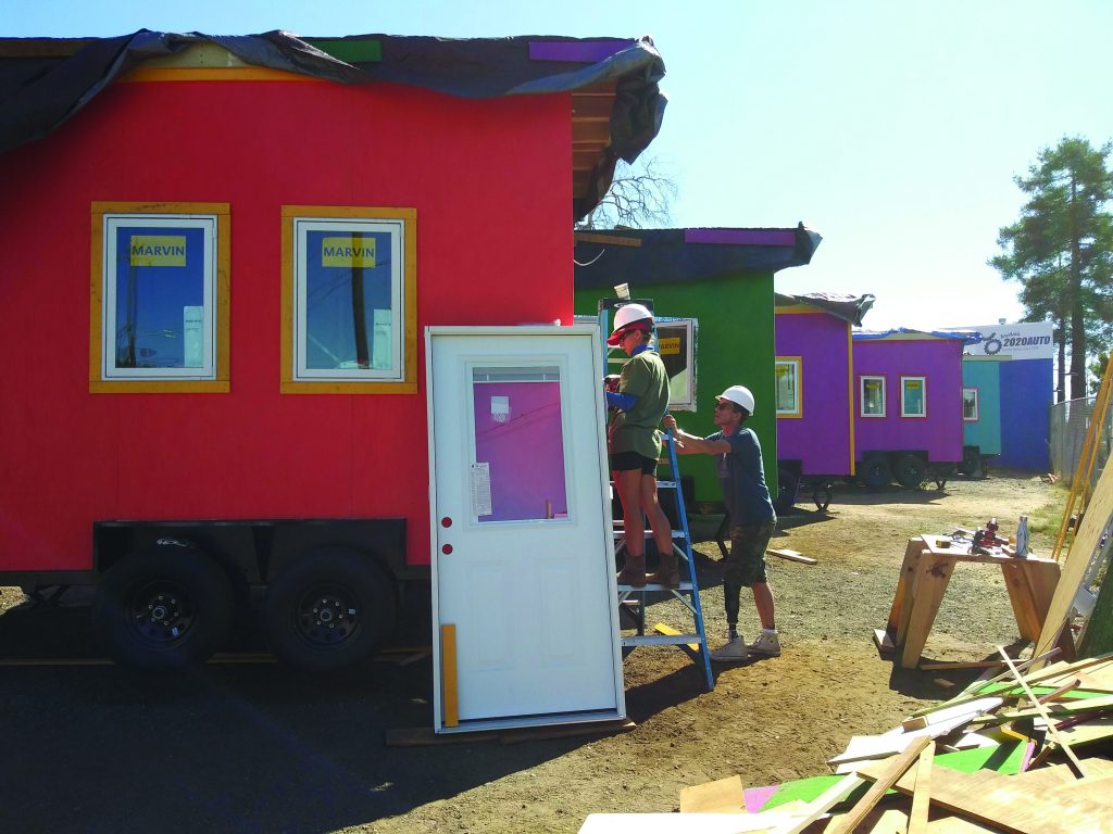 A row of multicolored tiny homes with volunteers working in the foreground. 