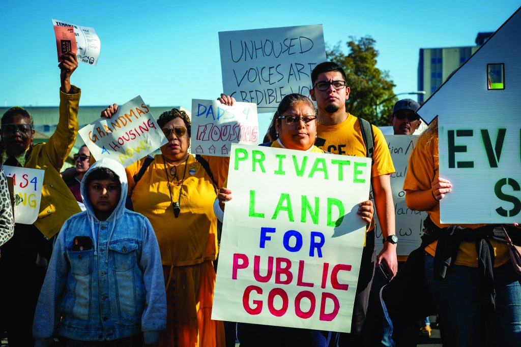 Protestors hold signs that read, "Private Land for Public Good" and "Unhouses Voices are credible now"