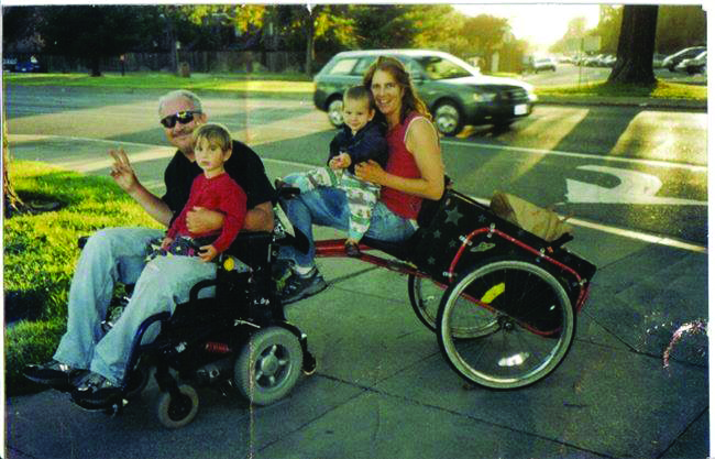 Danny and his wife, Katy, sit on his wheelchair with their two children.
