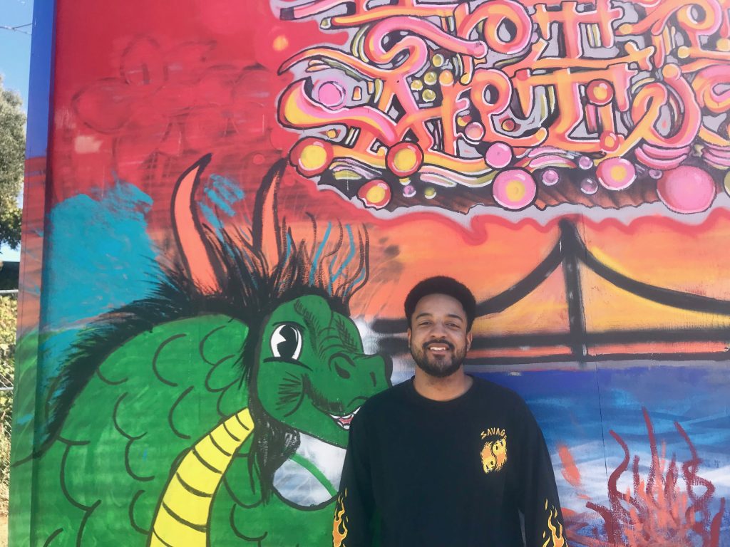 Reginald Gentry smiles for a photo in front of one of the tiny home murals.