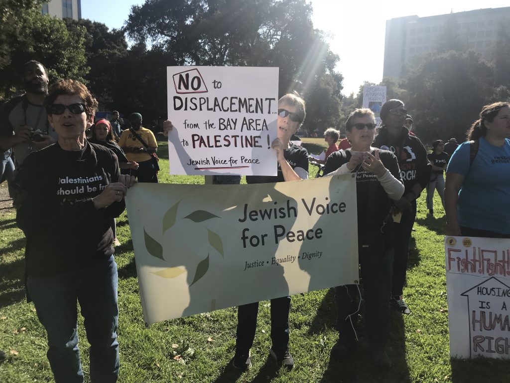Ellen Brotsky holds sign that says, "No to displacement from the Bay Area to Palestine. Jewish Voice for Peace". 