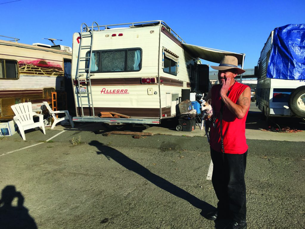 Jorge Peña holds his small dog in the parking space where his RV home is parked.