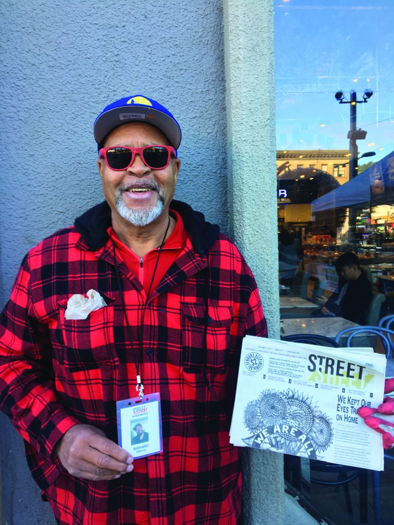 Marion Morris poses for a photo outside the Downtown Berkeley BART station, holing up a copy of Street Sheet.