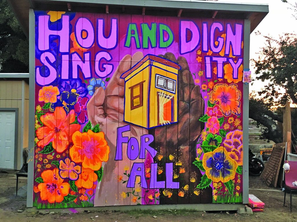 A mural by artist Ellie Hwa Brumbaum adorns one The Village’s latest guerilla tiny homes that reads, "Housing and Dignity for all". 