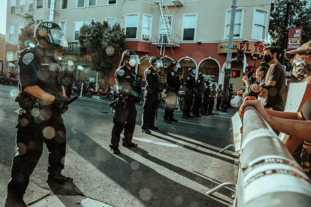 A line of police stand behind a barrier in front of protesters at the Mission police station.