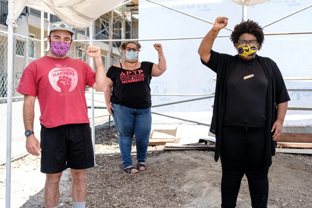 Three MH First volunteers pose for a photo wearing masks and holding up the fist of black power.