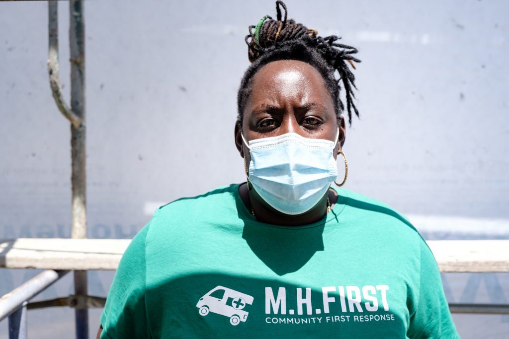 Mental Health First Program Coordinator Asantewaa Boikin wears a mask and a green shirt that says "MH First, community first response)