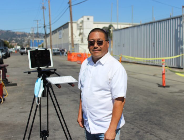 Derrick Soo, friend of Mike Lee, standing in front of an ipad propped up on a tripod, which he uses to do his broadcast “The Journey Home” about his experiences with homelessness.