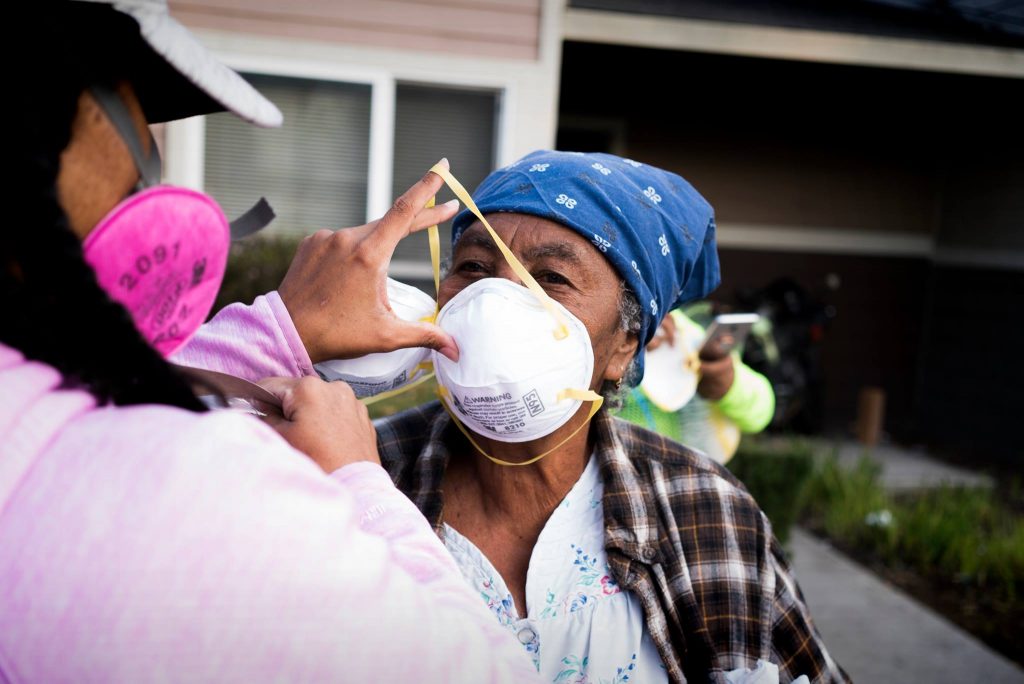 A volunteer gently puts a mask on an older woman's face.