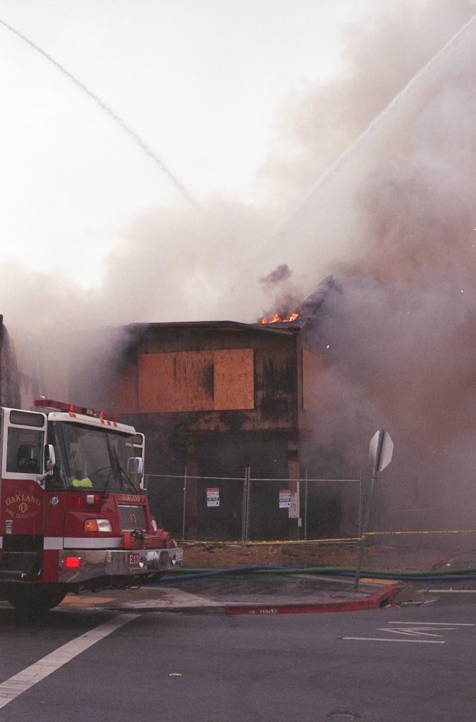 The Cryer Building is engulfed in pinkish smoke. On the left, the front of a fire engine can be seen.