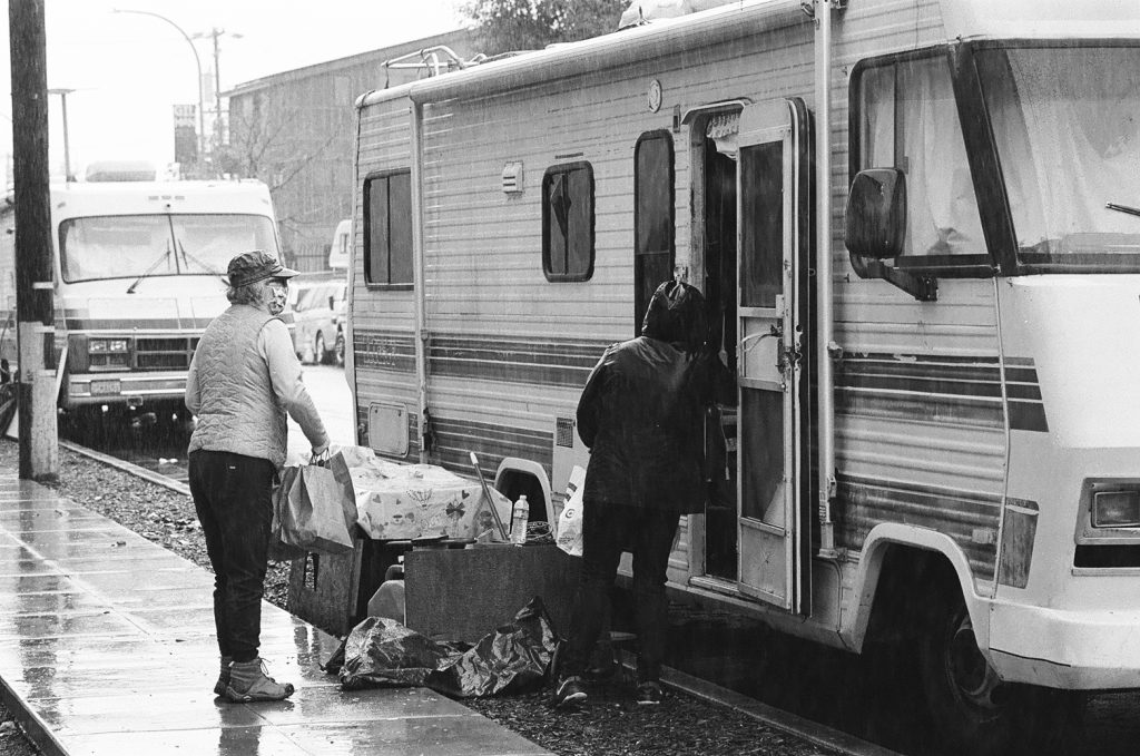 Prado and another volunteer hand supplies into the door of an RV. The road around them is wet.