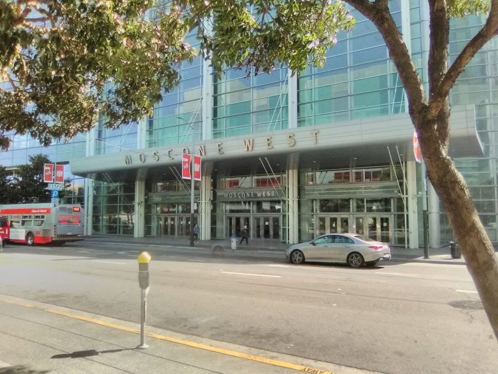 The front of San Francisco's Moscone West building. The building is modern with a blueish glass facade.