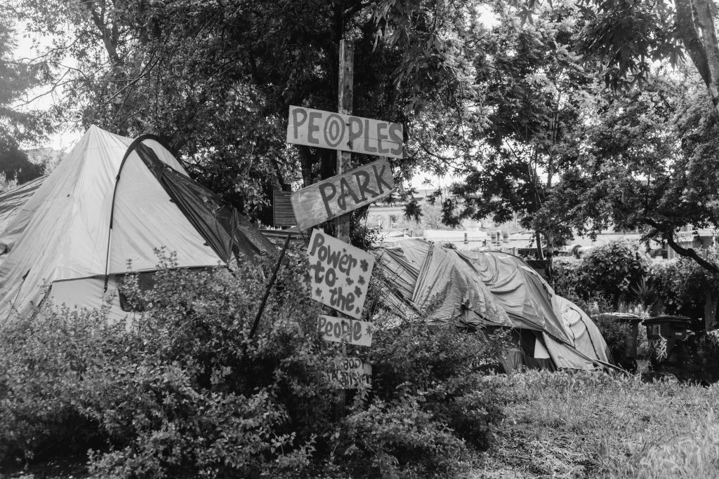 Tents can be seen in People's Park behind a series of signs that read "People's park, power to the people"