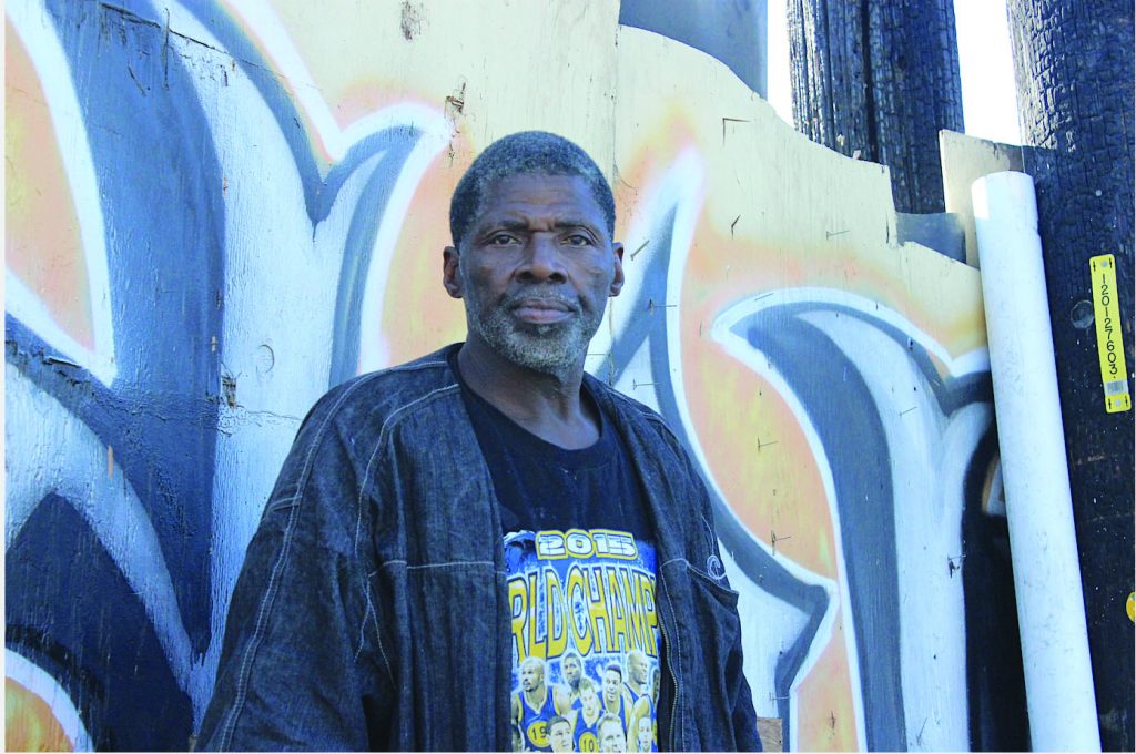 Jesse Parker, a Black man in his 50s, standing in front of an orange and black mural.
