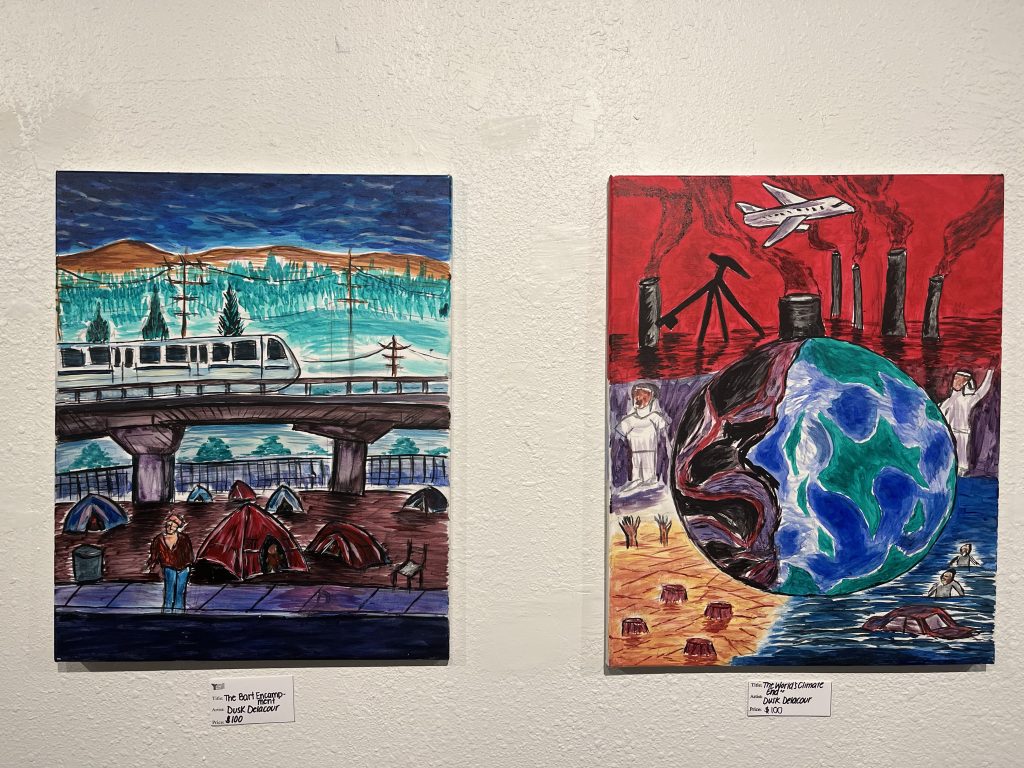 Two of Delacours paintings hang up side by side. The one on the left features a homeless encampment beneath a BART train, under an overpass. The one on the right depicts climate change. In the foreground planet earth is starting to become blackened. In the background the sky is red and studded with pipes that are spewing pollution into the air while a plane flies above.