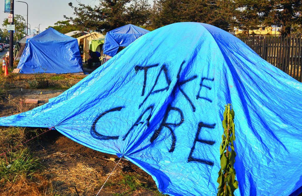 A tent that has a tarp over it with the words "take care" spray painted on the front.