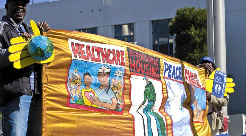 A banner carried by Oakland activists calls for health care, affordable housing, peace and food for all.