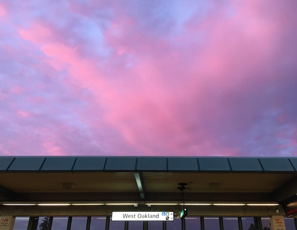 A pink and purple sky over a sign for the West Oakland BART station.