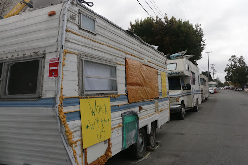A line of RVs along Eighth street. One of them has a sign taped to the side reading 