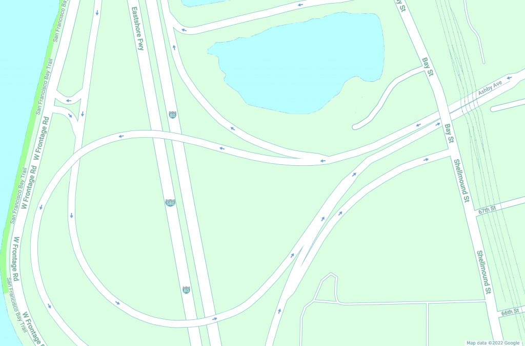 A straight forward google maps image of the encampment area from above. The land is represented by blocks of green, the water by blocks of blue, and the roads as white lines. The highway forms two thick stripes toward the left of the image, and the freeway offramp is a large circular loop that divides the land up into misshapen islands. 