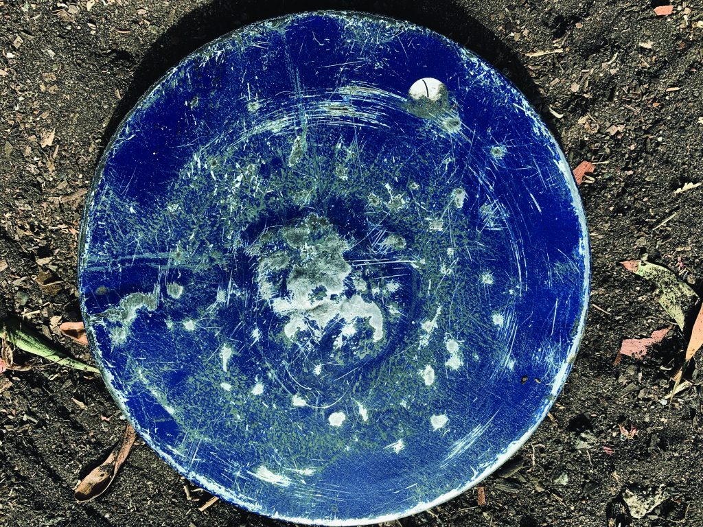 A round blue disk made out of metal that Ray uses as a drum. There are lots of raised and indented dots on the disk, where he has hit the disk with drumsticks.