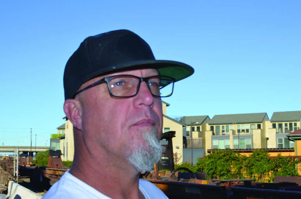 A portrait of Josh: a white man in his 40's waring black-rimmed, rectangular glasses, a black baseball cap, and a gray goatee.