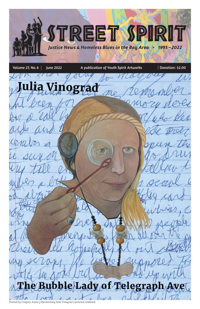 The June cover of Street Spirit: a page with scribbly blue handwriting on it. In front of the handwriting is a drawing of Julia Vinograd: an old white woman in a gold, tasseled hat, holding a bubble wand up to her eye. Her eye is framed by the bubble on the end of her wand.