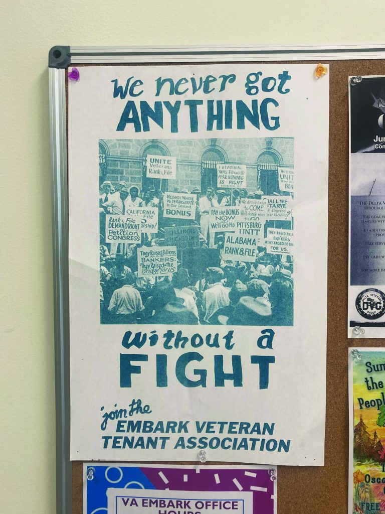 A poster on a community bulletin board says "we never go anything without a fight." it also contains an old photo of tenants organizing in Alabama, and the words "join the Embark Veteran Tenant Association."