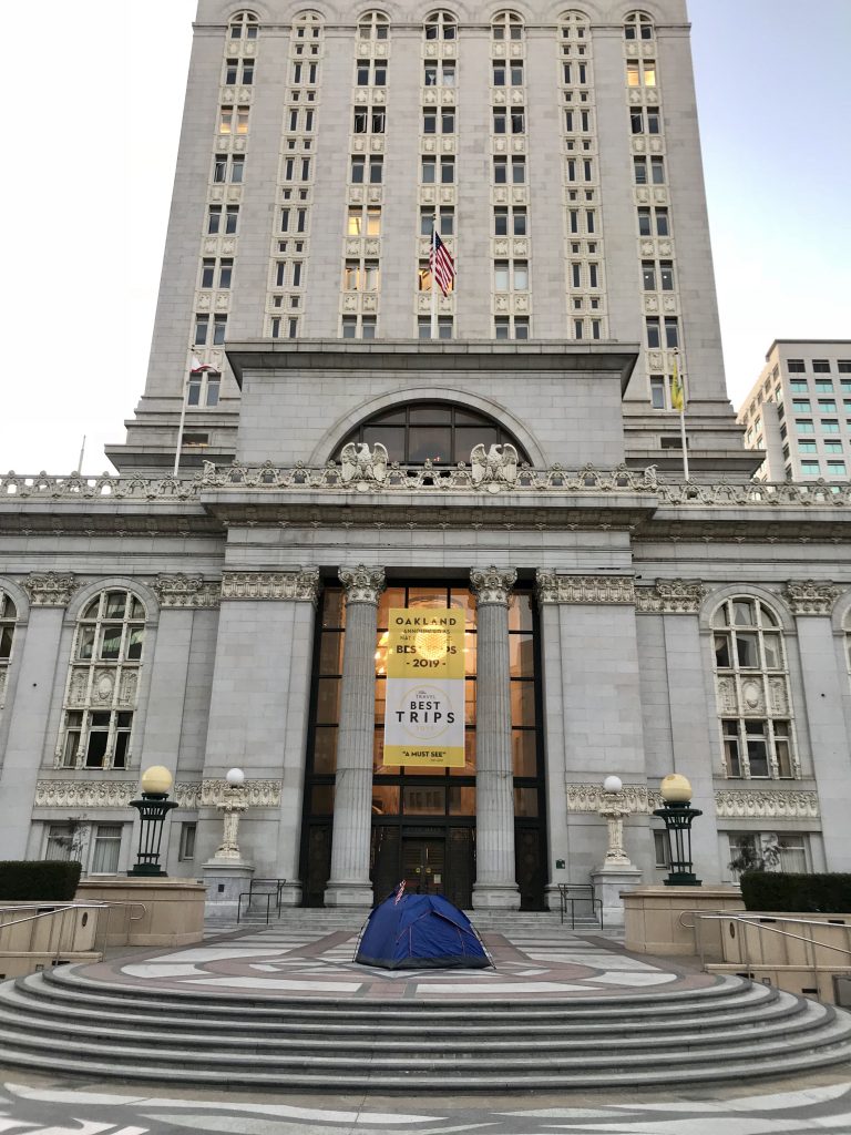 A single blue tent sits on the front steps of Oakland's City Hall building.