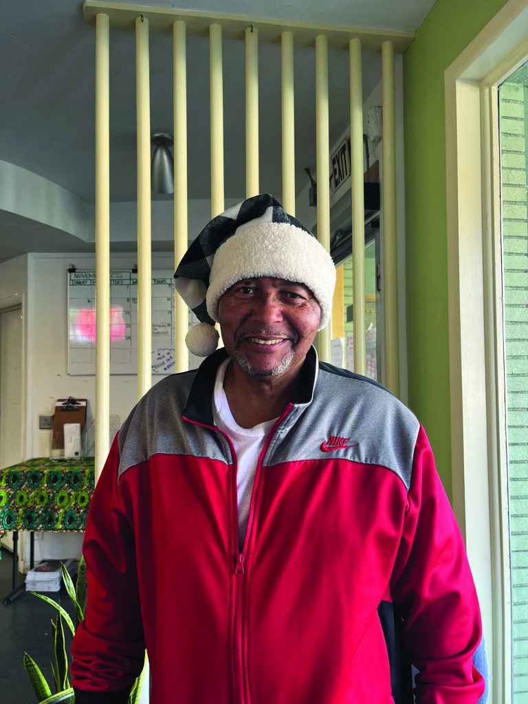 Street Spirit vendor Vernon Dailey, a Black man in a red Nike jacket wearing a gray plaid Santa hat.