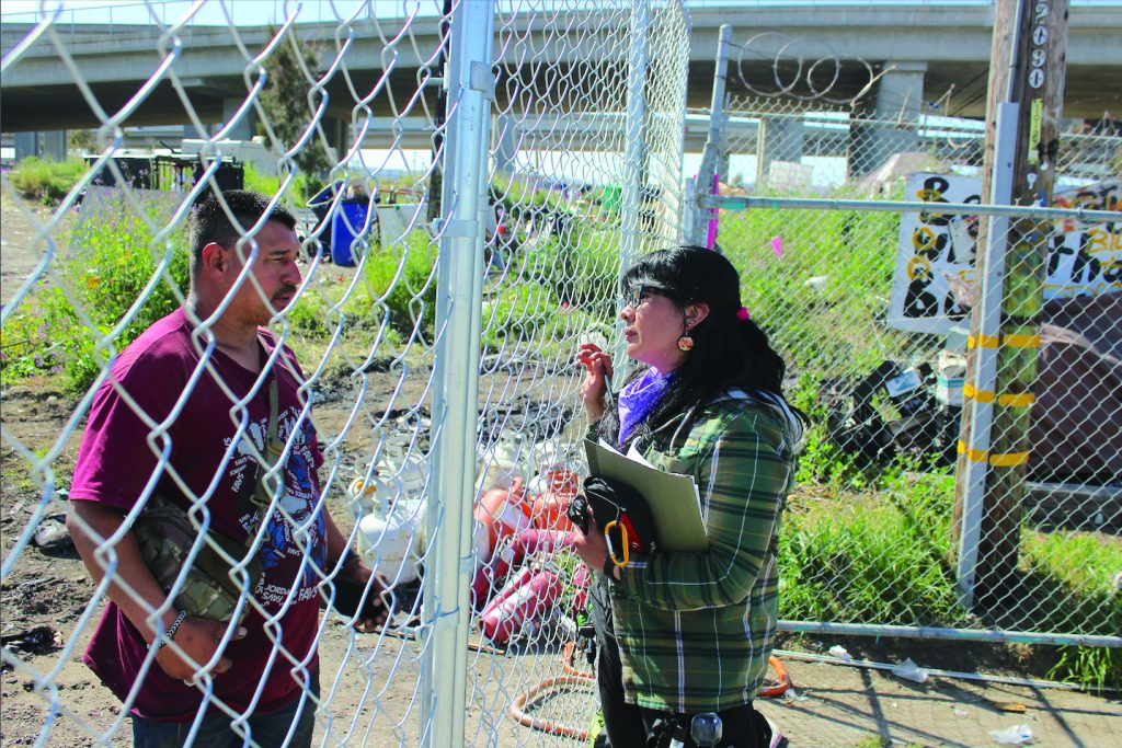 Yesica Prado interviews a resident of the Wood Street encampment through a chain link fence.