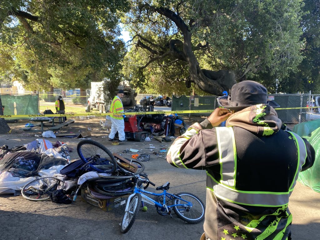 Oakland's Encampment Management Team surveys the remaining items of Shawn and Genea's camp, including a broken-down tent, suitcases, and bicycles.