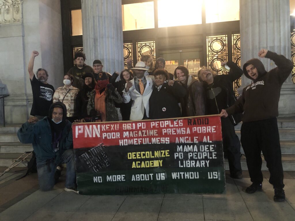 Members of Wood Street Community and Homefulness stand outside Oakland City Hall with their fists raised in solidarity with Palestine.